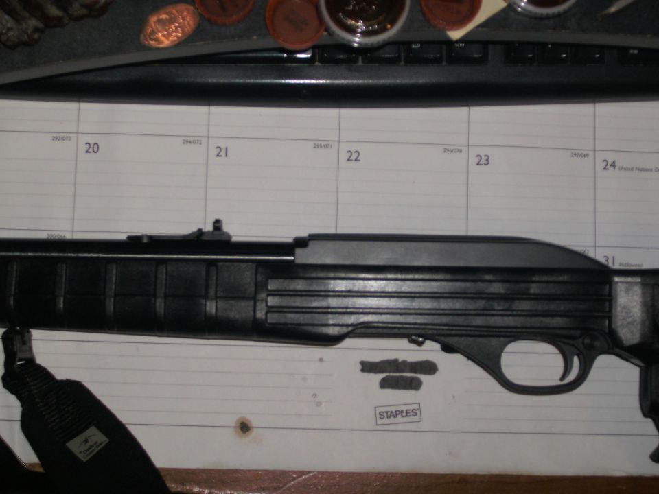 Black semi-auto rifle lying on a desk calendar with coins and keyboard nearby