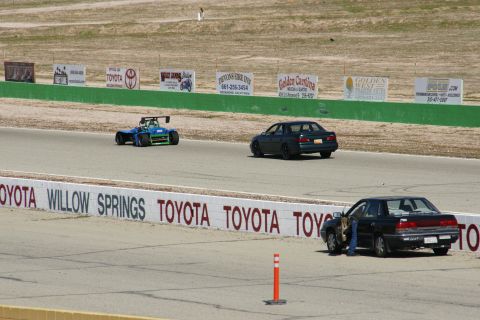 1995 Ford Taurus - A race track scene with multiple vehicles, including a dark sedan and a blue and green open-wheel car.
