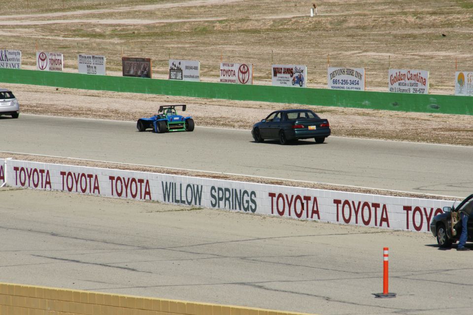 Dark sedan on race track with a blue open-wheel car