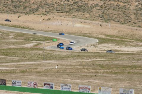 1995 Ford Taurus - Multiple vehicles navigate a challenging race track under a bright sky, with spectators visible in the distance.