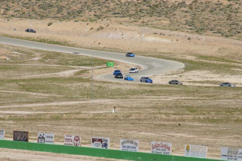 1995 Ford Taurus - Multiple cars are racing on a track in a dry, hilly area. Signs line the bottom of the frame.
