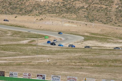 1995 Ford Taurus - Several cars are driving on a race track in a desert-like environment with spectators' banners in the foreground.