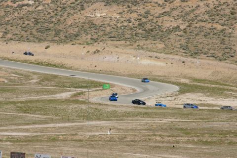 1995 Ford Taurus - Several cars are seen navigating a serpentine race track under a bright sky, with arid hills in the background.
