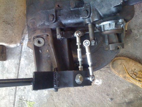 1978 Ford Bronco - Close-up of a vehicle's transfer case linkage, showing mechanical components and a shoe in the background.
