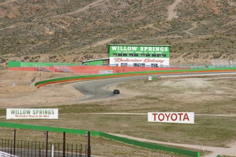 1995 Ford Taurus - A lone dark sedan navigates a turn on the Willow Springs race track, with prominent signage in the background.