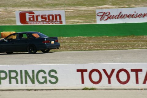 1995 Ford Taurus - A dark sedan is seen on a race track, with sponsor advertisements visible in the background.