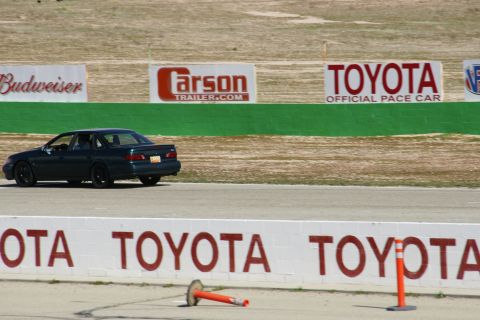 1995 Ford Taurus - A dark sedan is seen on a race track with advertising banners in the background.
