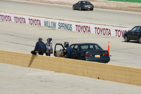 1995 Ford Taurus - A 1995 Ford Taurus is seen on a race track with people gathered around its open door, with other vehicles in the background.