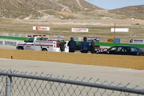 1995 Ford Taurus - A service truck and two cars are present at a race track, with several individuals observing the scene.