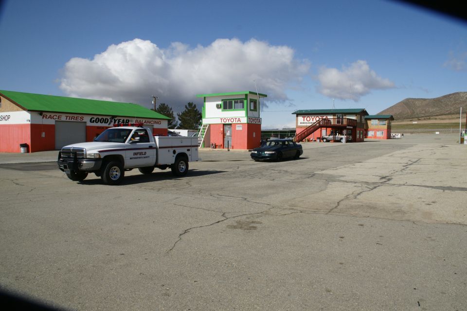 White pickup truck and dark sedan on a paved lot with buildings and mountains in the background