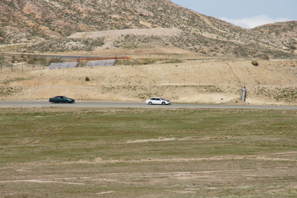 Two sedans drive on a road through a dry, hilly landscape with sparse vegetation