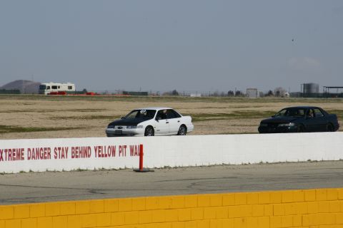 1995 Ford Taurus - Two sedans are on a race track, with an RV visible in the distance behind a safety wall.