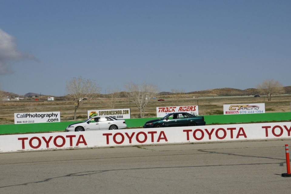 Two sedans race on a track with Toyota branding on the wall