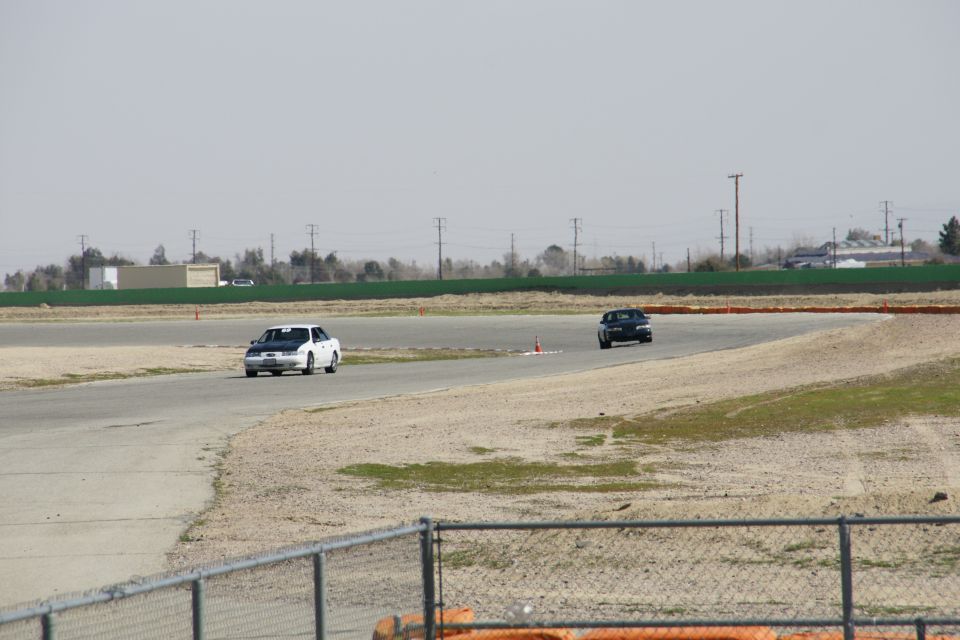 White 1995 Ford Taurus with black hood on racetrack, front view