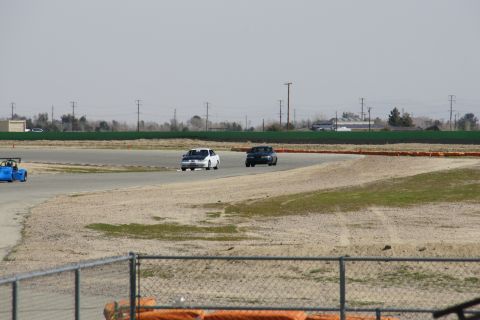 1995 Ford Taurus - Multiple vehicles race on a track with a dusty infield and distant buildings.