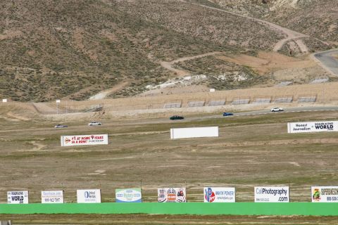 1995 Ford Taurus - Multiple vehicles race on a track surrounded by arid hills, with numerous sponsor billboards visible in the foreground.