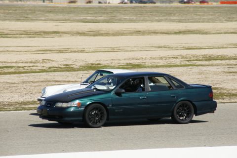 1995 Ford Taurus - A green sedan and a white car are driving on a race track.