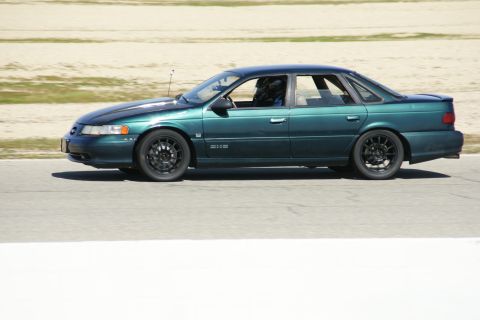 1995 Ford Taurus - A green 1995 Ford Taurus sedan is captured in profile on a race track.