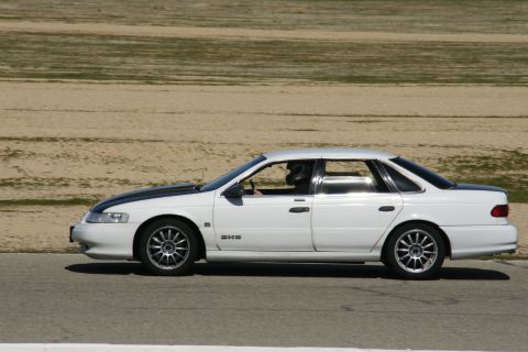 1995 Ford Taurus - A white 1995 Ford Taurus sedan with a black hood stripe is seen on a track, likely participating in a racing event.