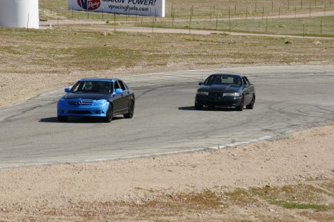 1995 Ford Taurus - Two sedans are driving on a race track during a sunny day.