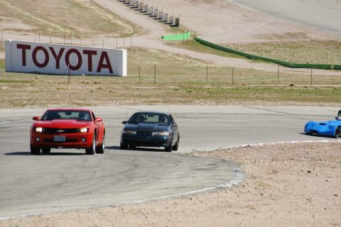 1995 Ford Taurus - Three cars are on a race track, with a large TOYOTA sign visible in the distance.