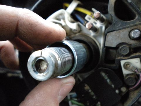 1989 Ford Bronco - A finger points to the threaded shaft of a steering column ignition switch mechanism, with wiring visible in the background.