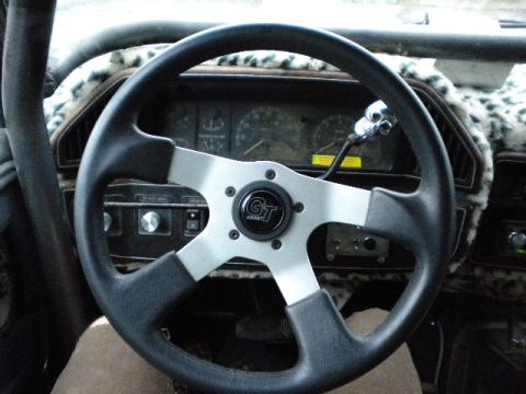 1989 Ford Bronco - The dashboard and steering wheel of a vehicle, an aftermarket Grant steering wheel and a leopard print dash cover.