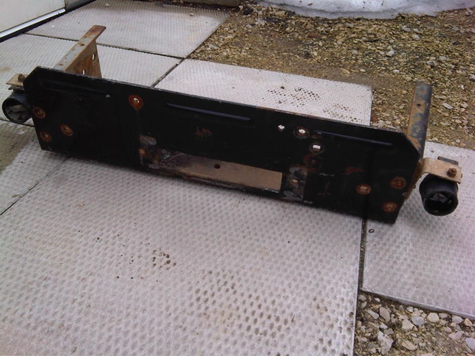 Truck bumper bracket, black metal with rust, on a tiled surface