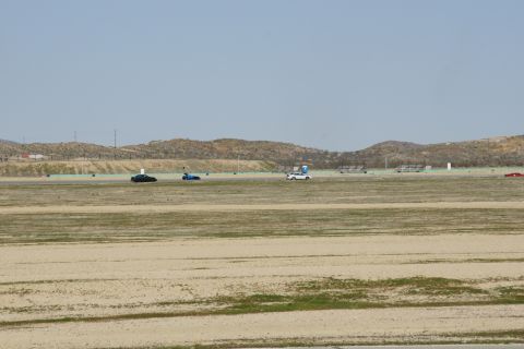 1995 Ford Taurus - Multiple vehicles are visible on a track under a hazy sky, with distant hills and structures.