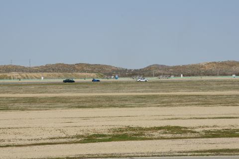 1995 Ford Taurus - A black sedan, blue sports car, and white SUV are visible on a track with arid hills under a hazy sky.
