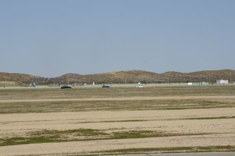 1995 Ford Taurus - Several vehicles are on a track with a dry, hilly landscape under a clear blue sky.