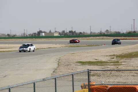 1995 Ford Taurus - A white sedan with a black hood drives on a racetrack alongside other vehicles.