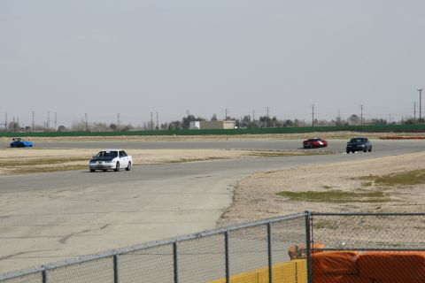 1995 Ford Taurus - Multiple vehicles race on a track under a hazy sky.