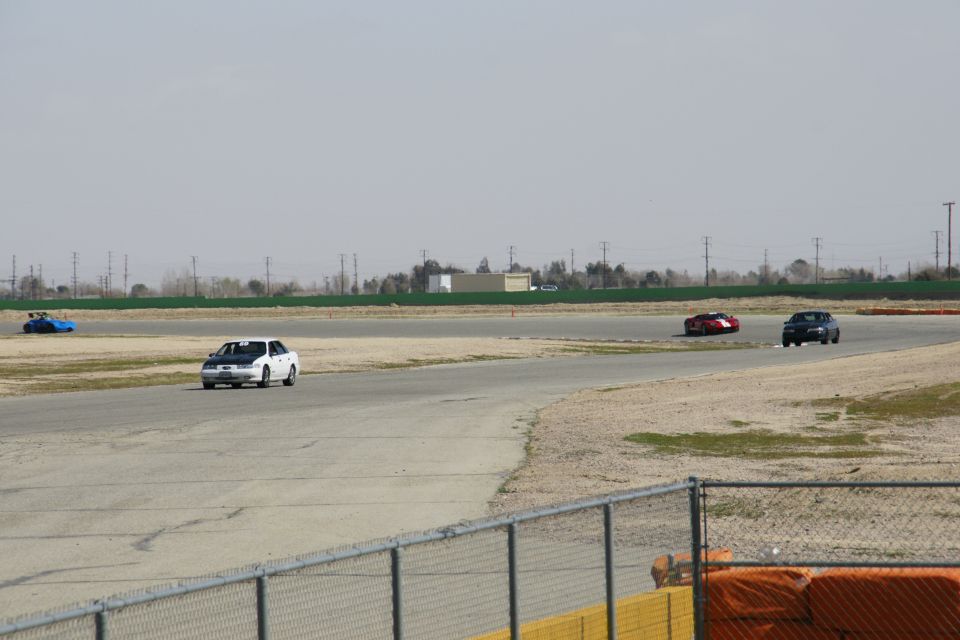 White sedan on a race track with a blue car and two other cars in the distance
