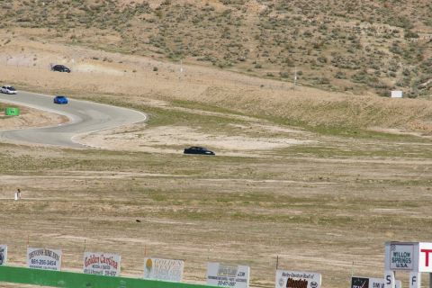 1995 Ford Taurus - Multiple cars race on a track with dry, hilly terrain and sponsor signs in the foreground.