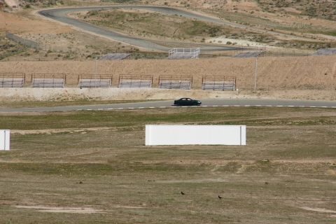 1995 Ford Taurus - A dark sedan travels along a race track in a dry, hilly landscape.
