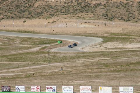 1995 Ford Taurus - Two cars navigate a sweeping turn on a dry, dusty race track under a clear sky.