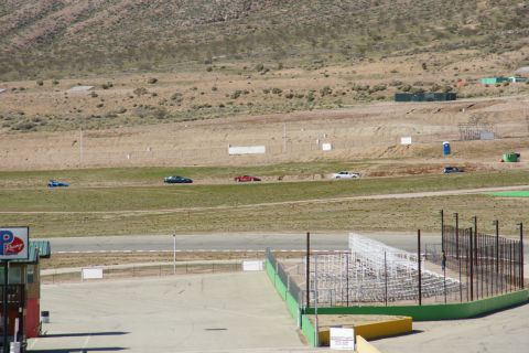 1995 Ford Taurus - Several cars are driving on a race track in a dry, hilly landscape.