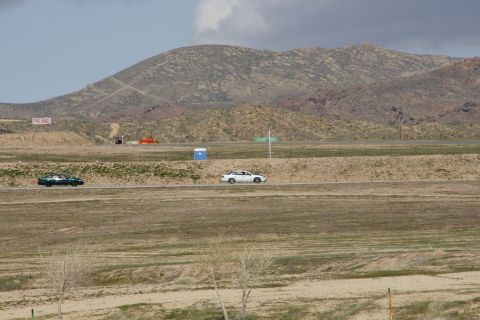 1995 Ford Taurus - Two cars drive on a road with a portable toilet and distant mountains under a cloudy sky.