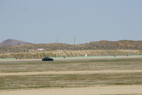 1995 Ford Taurus - A dark sedan is seen on a race track, with dry, rolling hills and power lines visible in the distance under a clear sky.