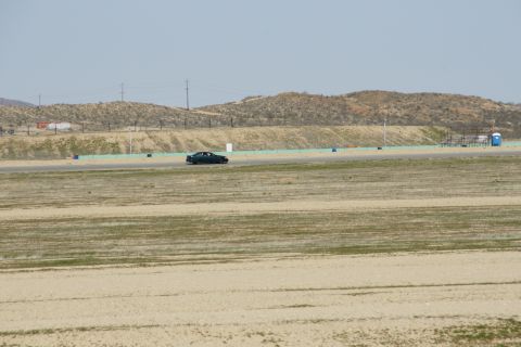 1995 Ford Taurus - A dark sedan is seen on a race track with a barren landscape and hills in the distance.