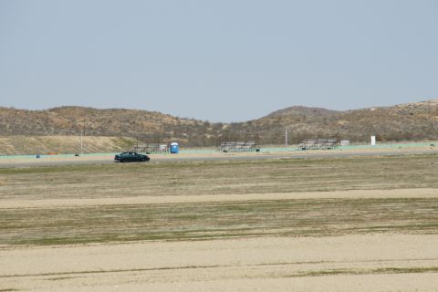 1995 Ford Taurus - A lone dark sedan drives on a race track under a clear sky.