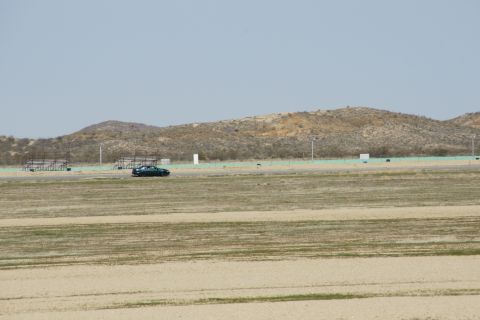 1995 Ford Taurus - A dark sedan is seen driving on a racetrack with arid hills and empty bleachers under a clear sky.