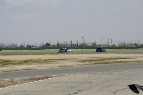1995 Ford Taurus - Two cars are on a paved track with grassy areas and utility poles in the background under a cloudy sky.