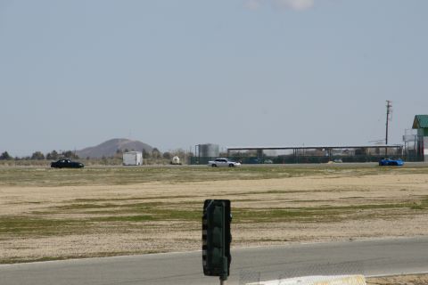1995 Ford Taurus - Cars are seen driving on a racetrack under a clear sky with distant hills and structures.