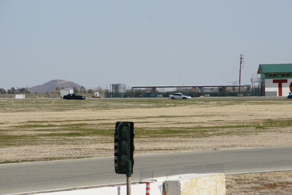 Two sedans drive on a race track with a traffic light in the foreground