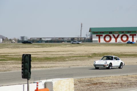1995 Ford Taurus - A white coupe drives on a track near a building with TOYOTA painted on it.