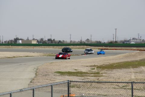 1995 Ford Taurus - Cars compete on a paved race track with a chain-link fence in the foreground.