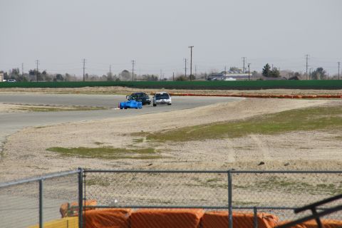 1995 Ford Taurus - A blue race car and a white sedan are seen on a race track during an event.