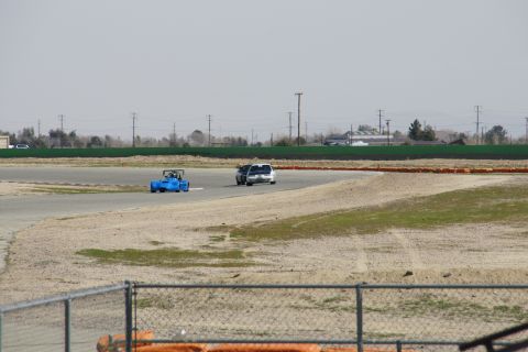 1995 Ford Taurus - Two vehicles compete on a paved racetrack under a hazy sky.